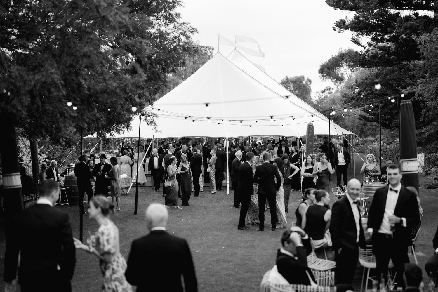 Black and white photo showing a gathering of people under a large white tent at an outdoor social event or celebration.