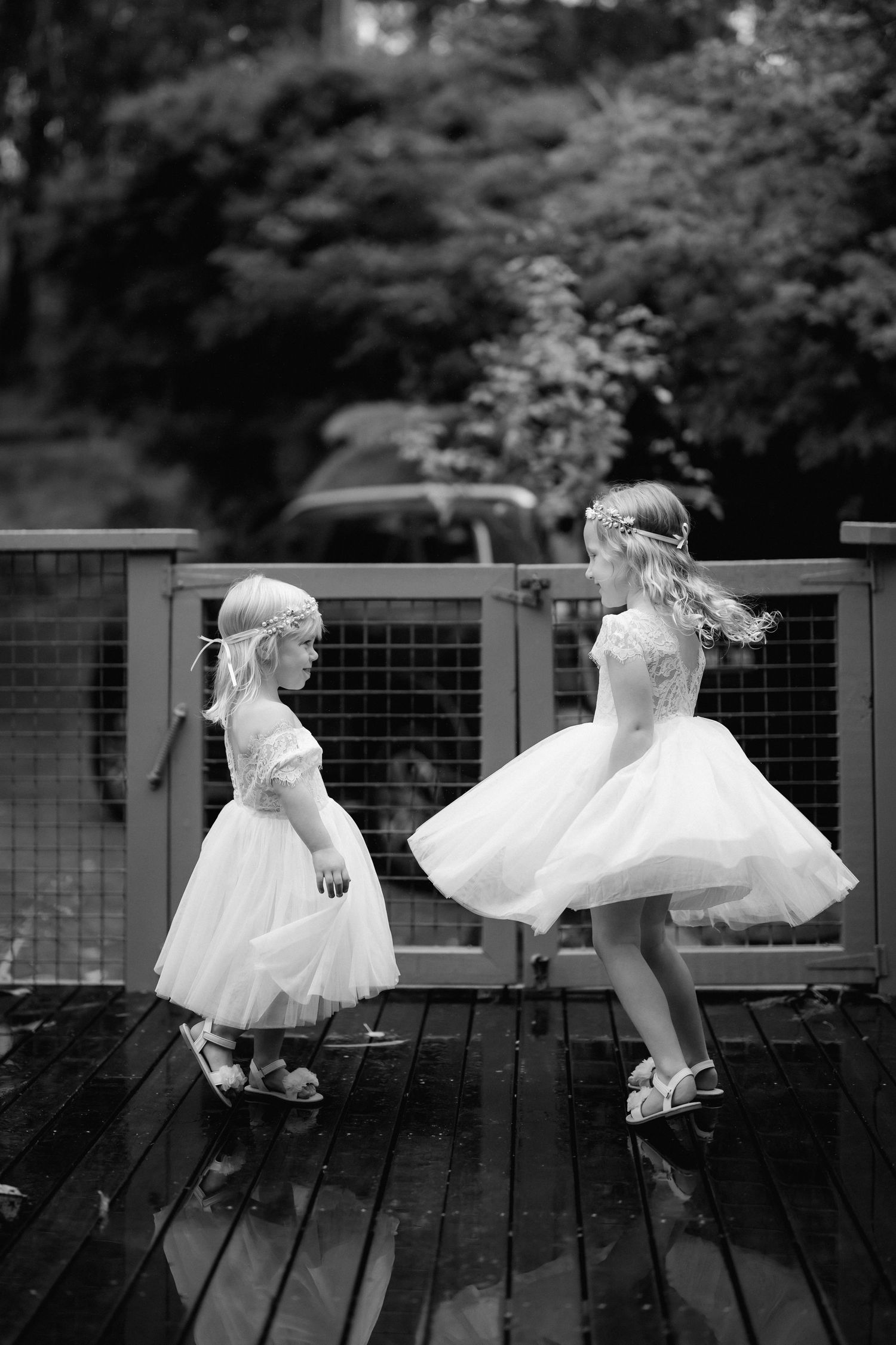 Two children in white tulle dresses twirling and dancing together on a wooden deck in black and white photography.
