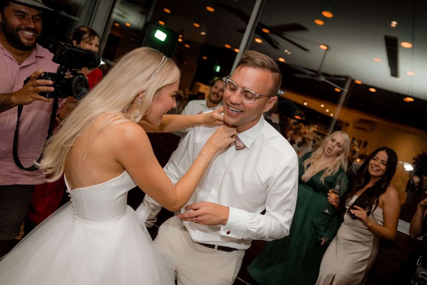 Wedding guests dancing and celebrating at a dimly lit evening reception.