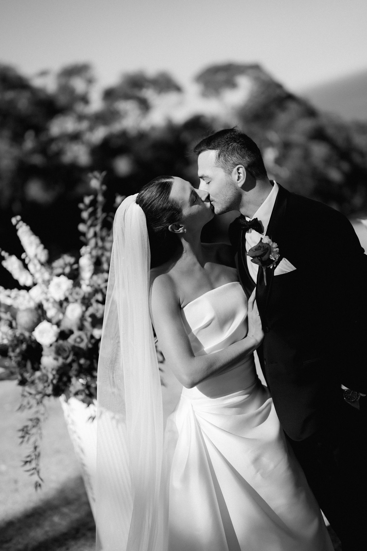 A romantic black and white wedding photo sequence showing the couple kissing outdoors with floral arrangements.