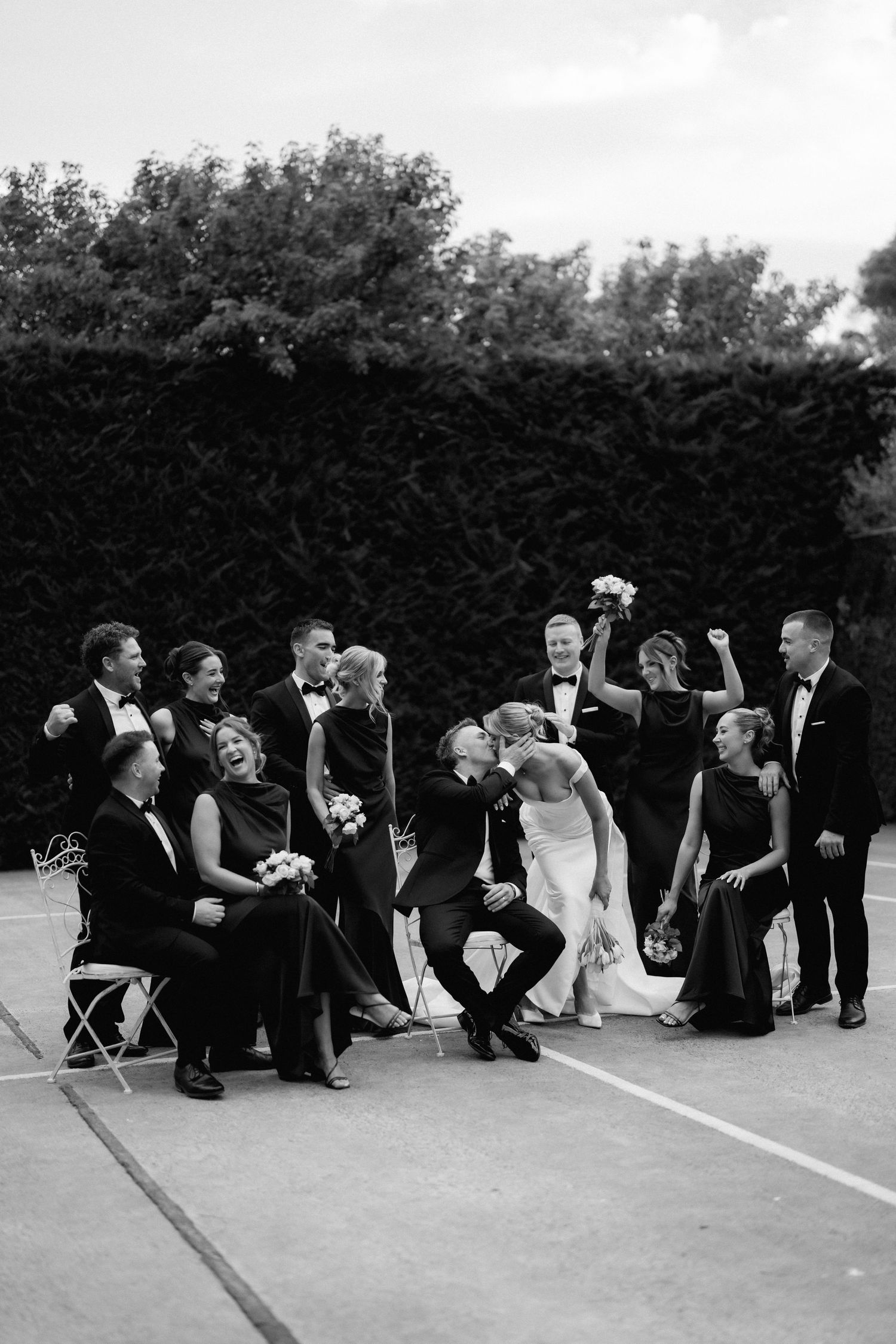 Wedding party poses casually on ground in black and white group photo.