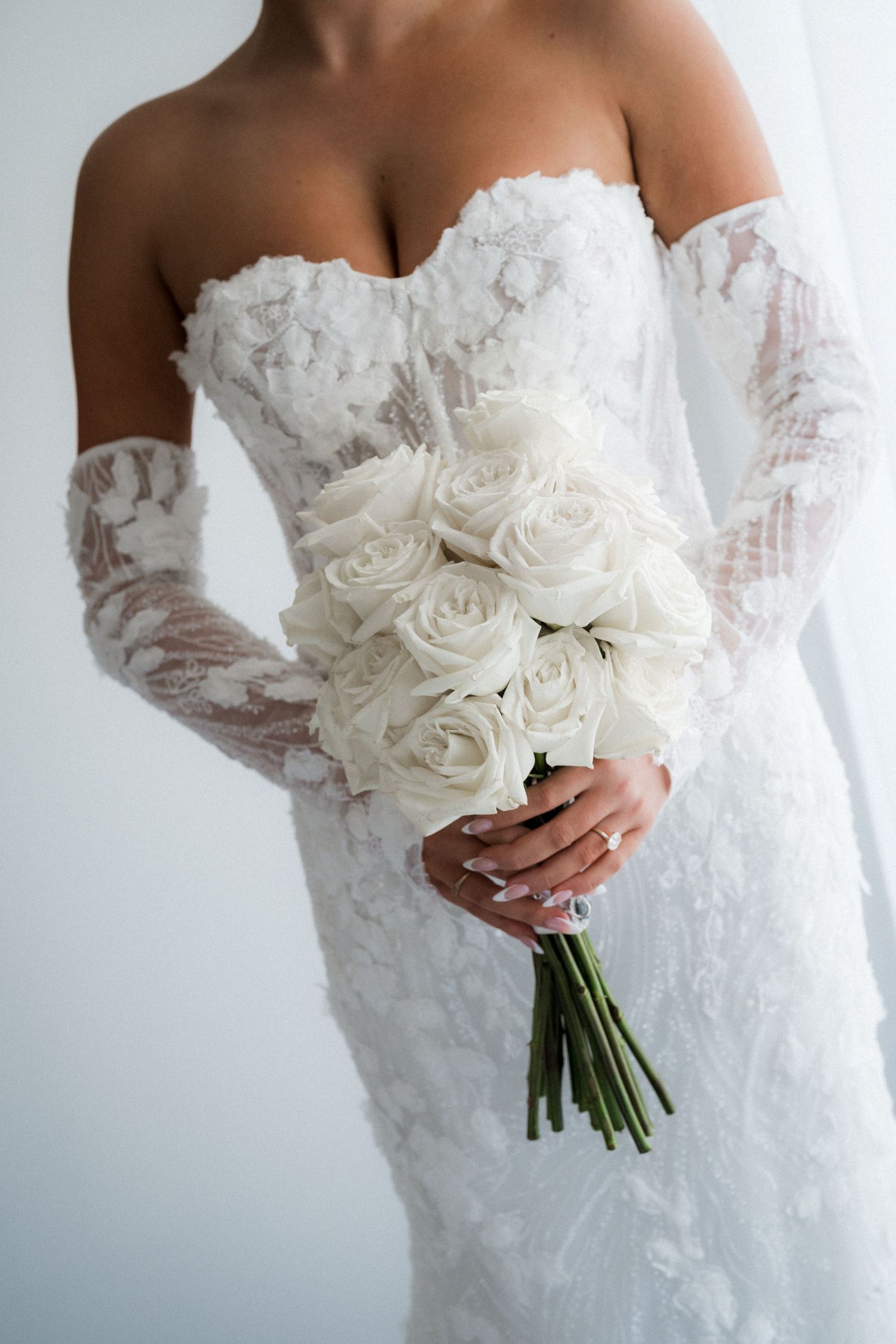 White bridal bouquet of roses held against a lace wedding dress in elegant detail shots.