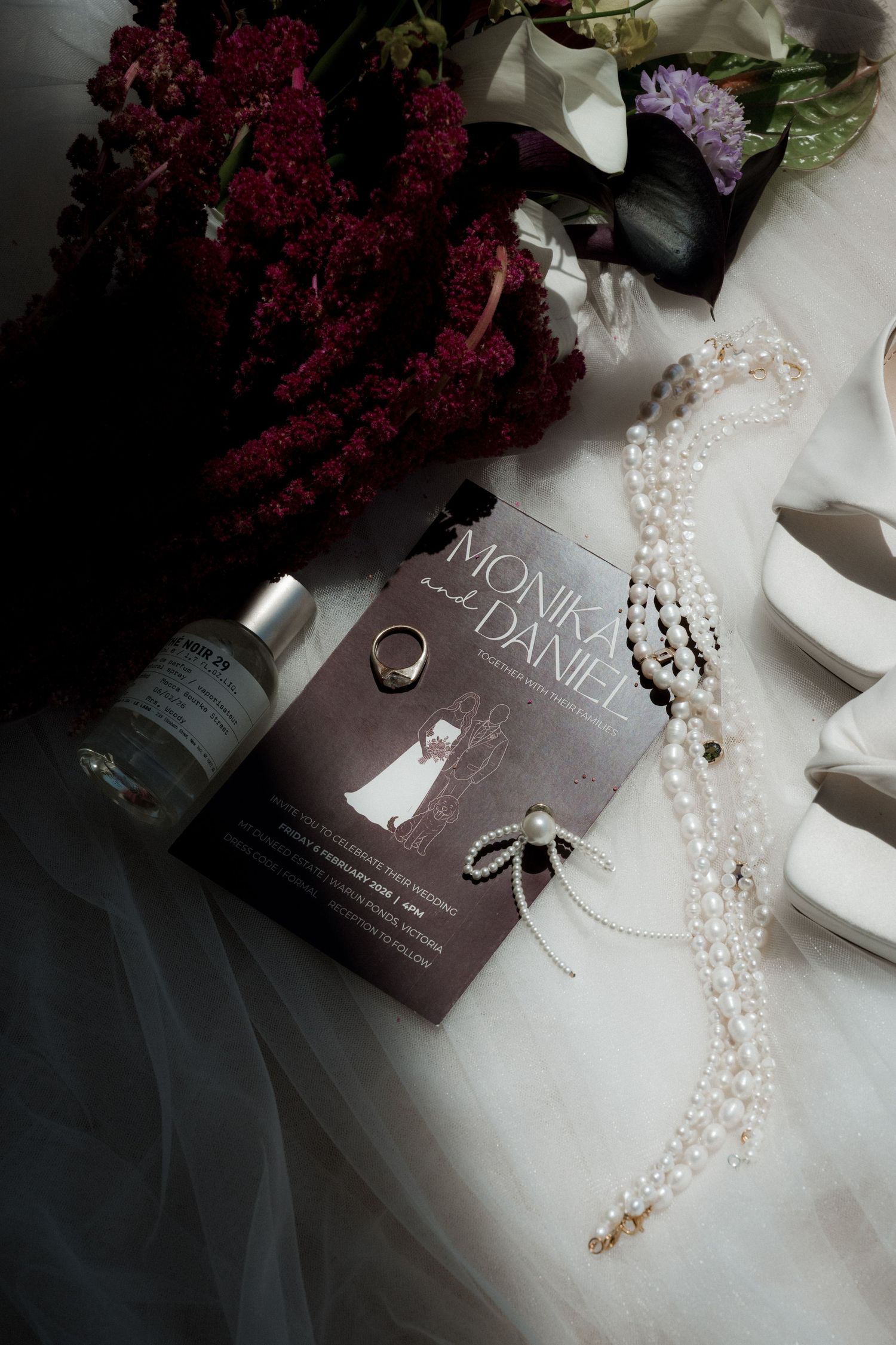 Wedding accessories including pearl necklace and invitation cards arranged with burgundy flowers.