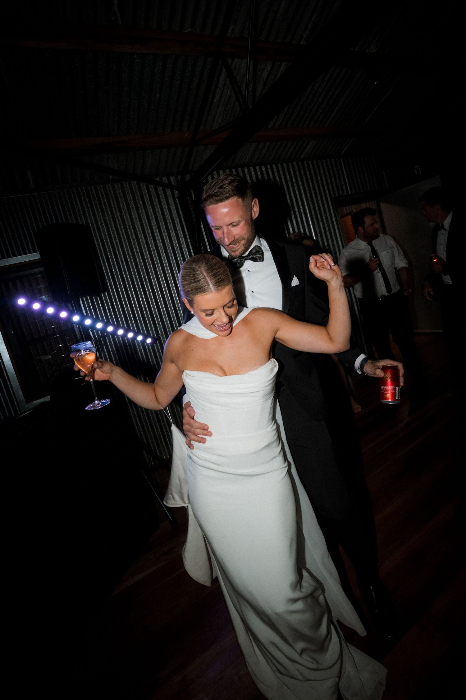 Newlyweds share energetic dance moves on a dimly lit reception dance floor.