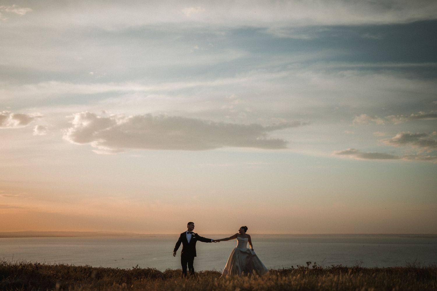 Dramatic sunset silhouettes against cloudy sky during outdoor wedding photography.