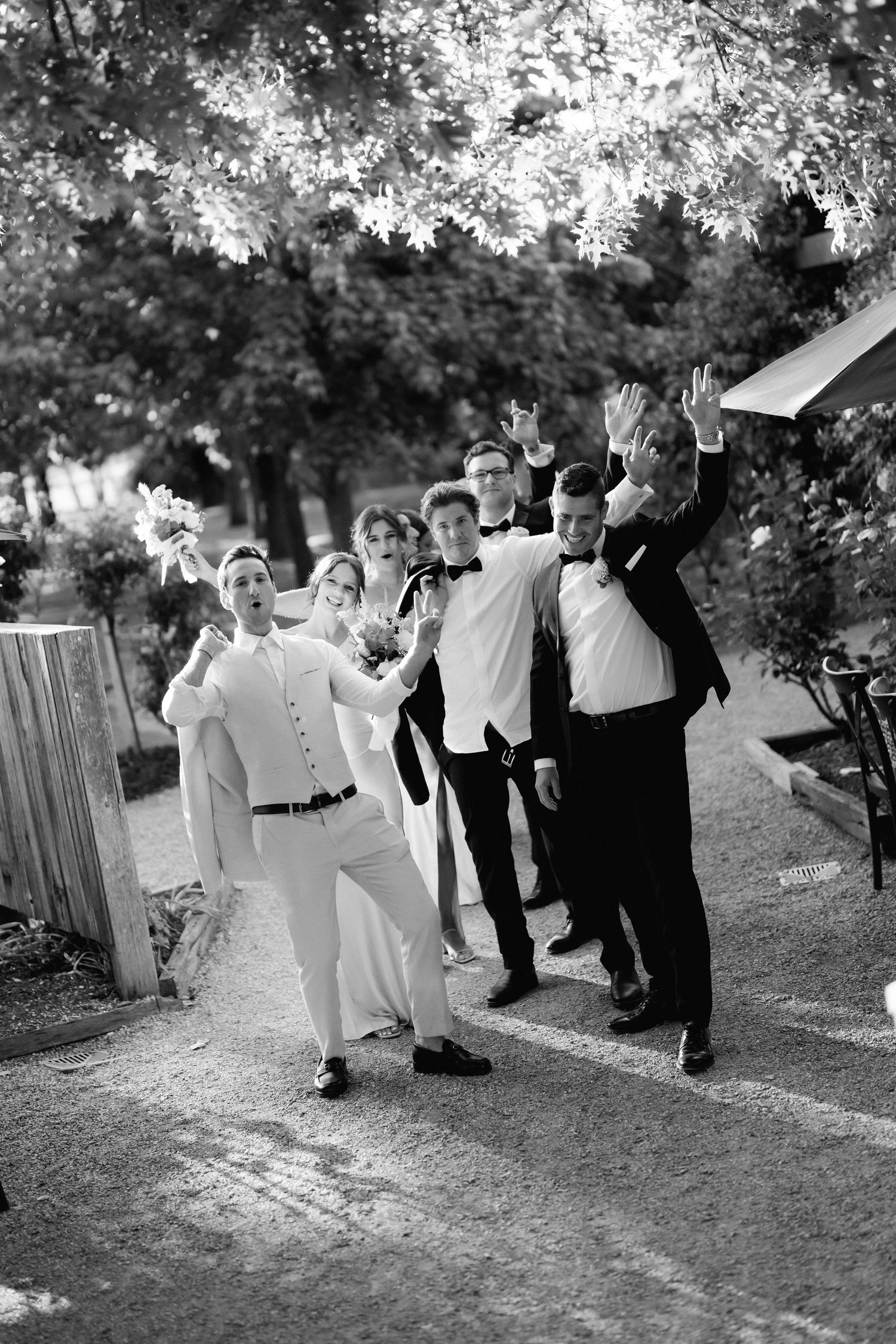 Joyful wedding party jumping and celebrating outdoors in a candid black and white photo.