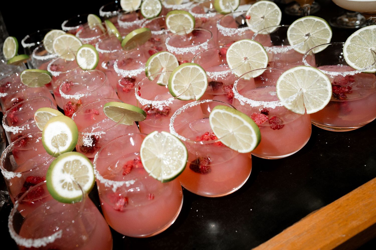 Row of pink cocktails garnished with fresh lemon slices on dark surface.