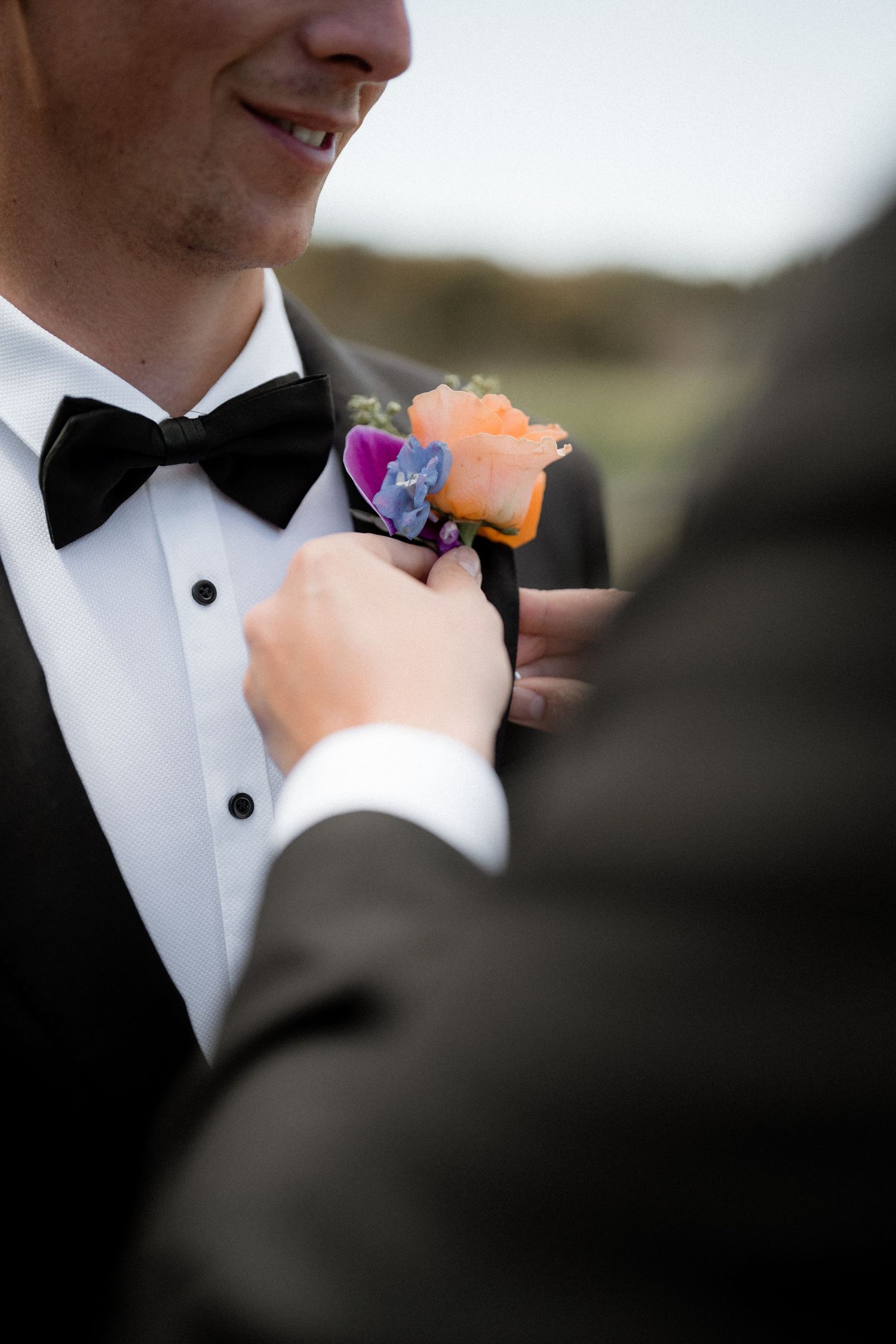 Closeup series of groom in black tuxedo and bowtie pinning on a colorful boutonniere.