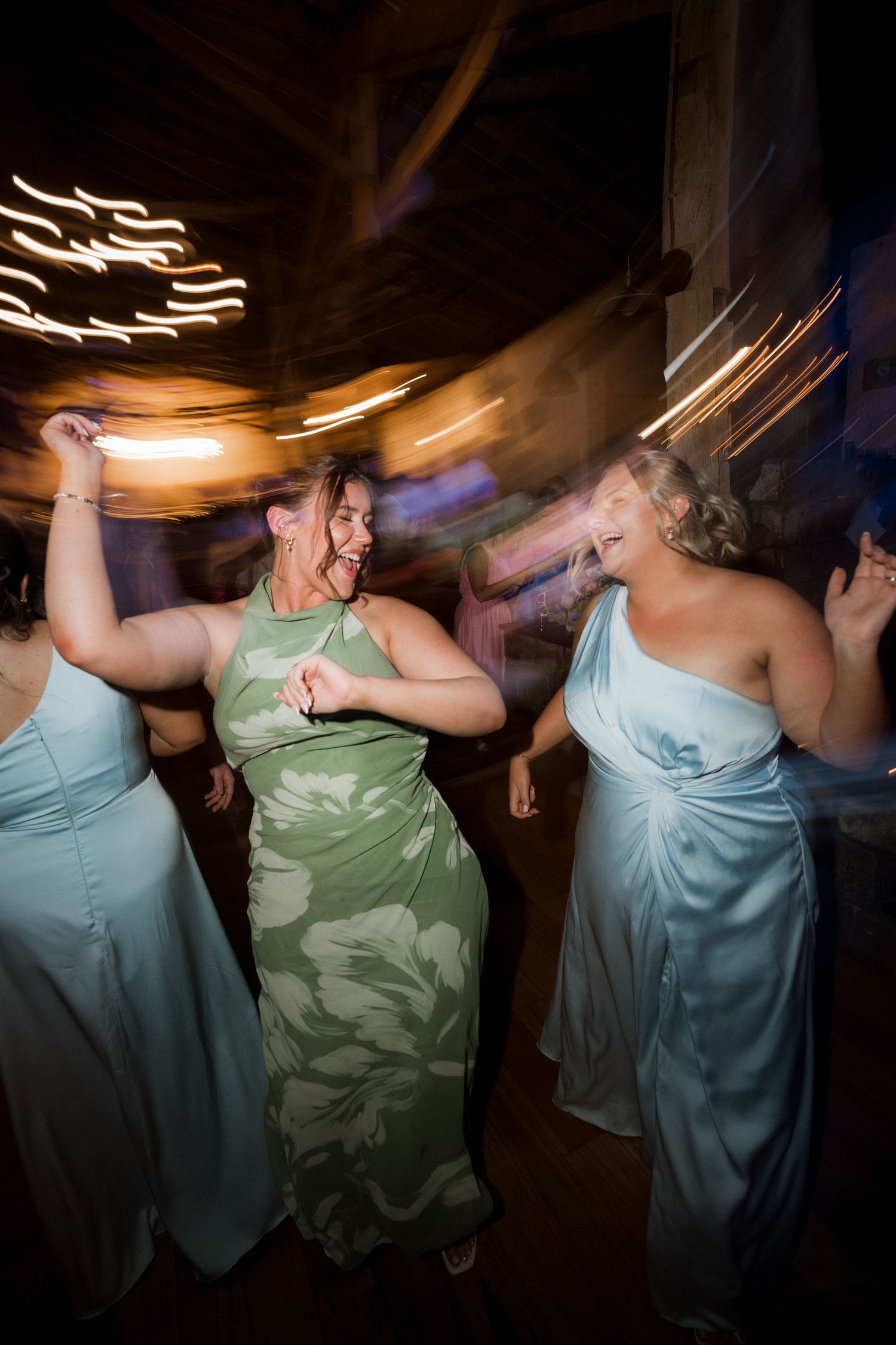 Bridesmaids in light blue dresses dance energetically at a lively wedding reception.