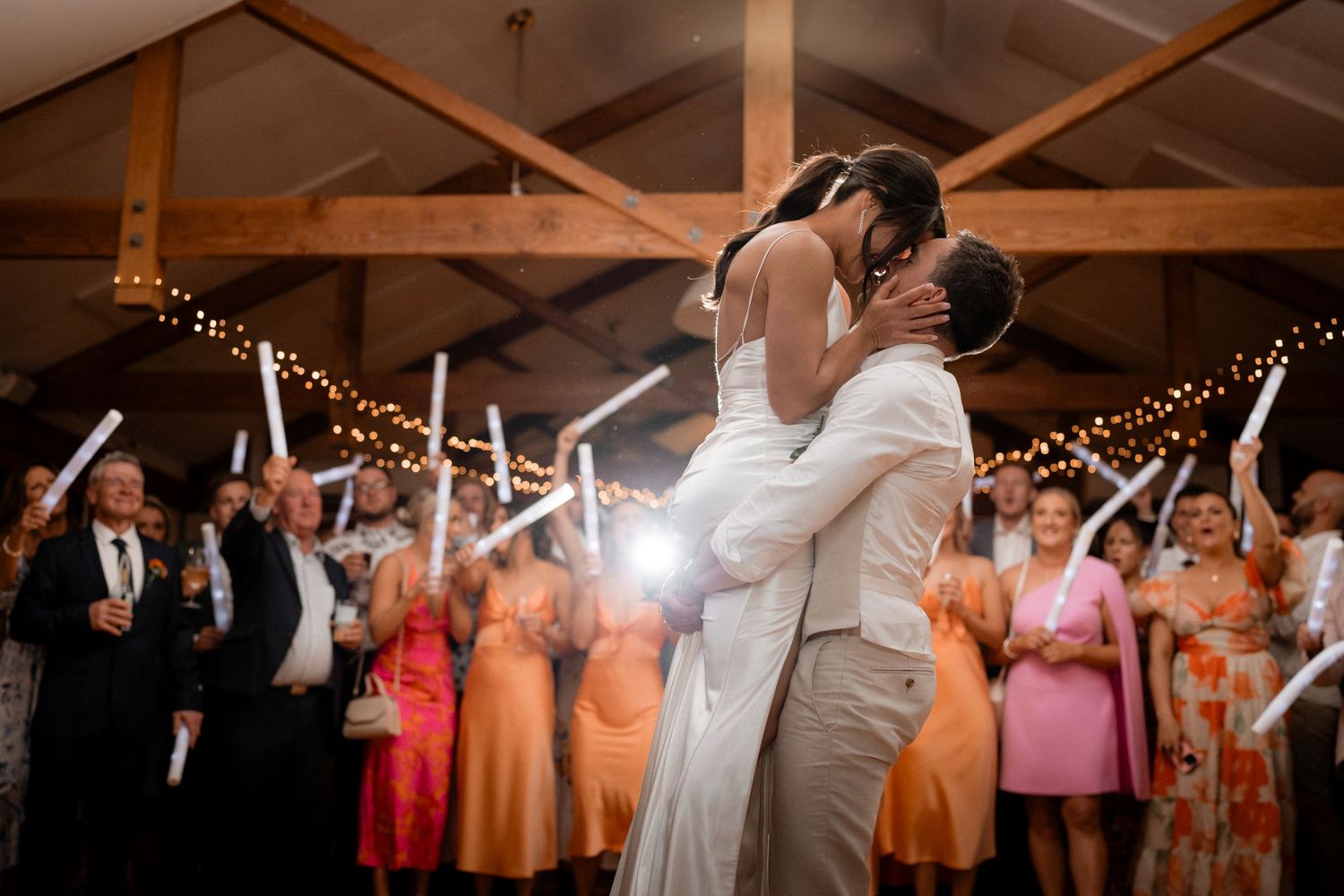 Wedding guests dancing and celebrating under string lights in a rustic barn venue.
