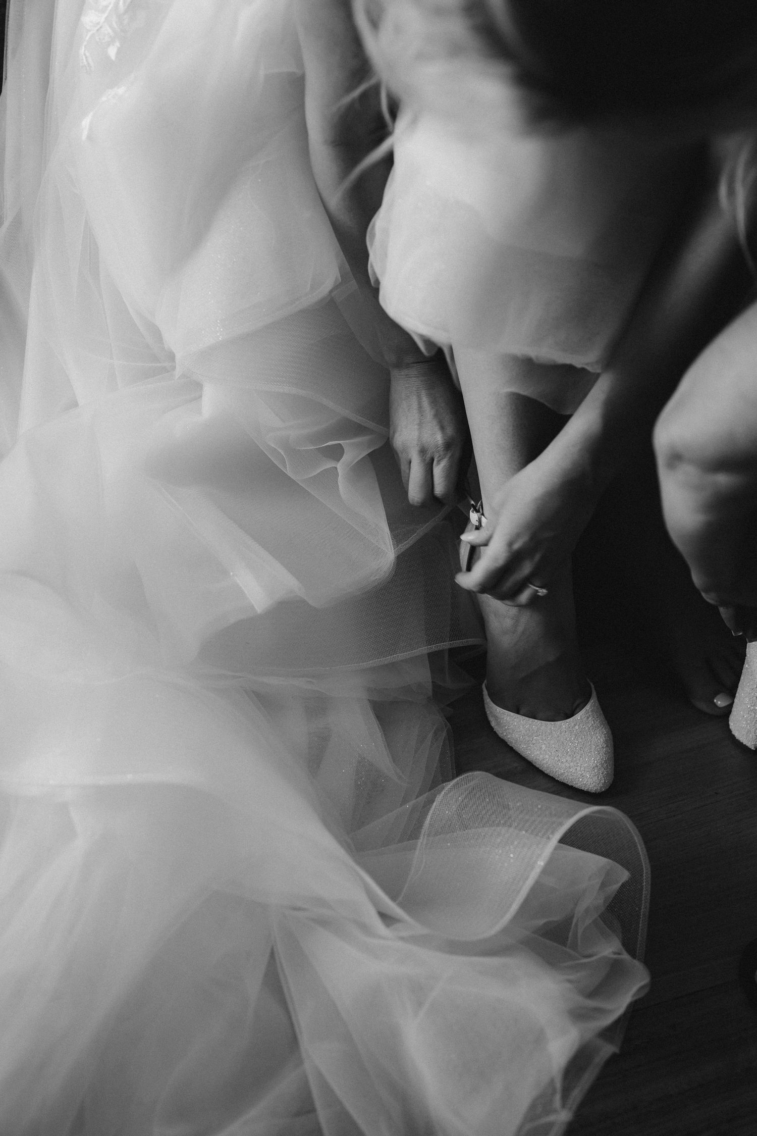 Black and white detail shot of bride putting on white wedding shoes.