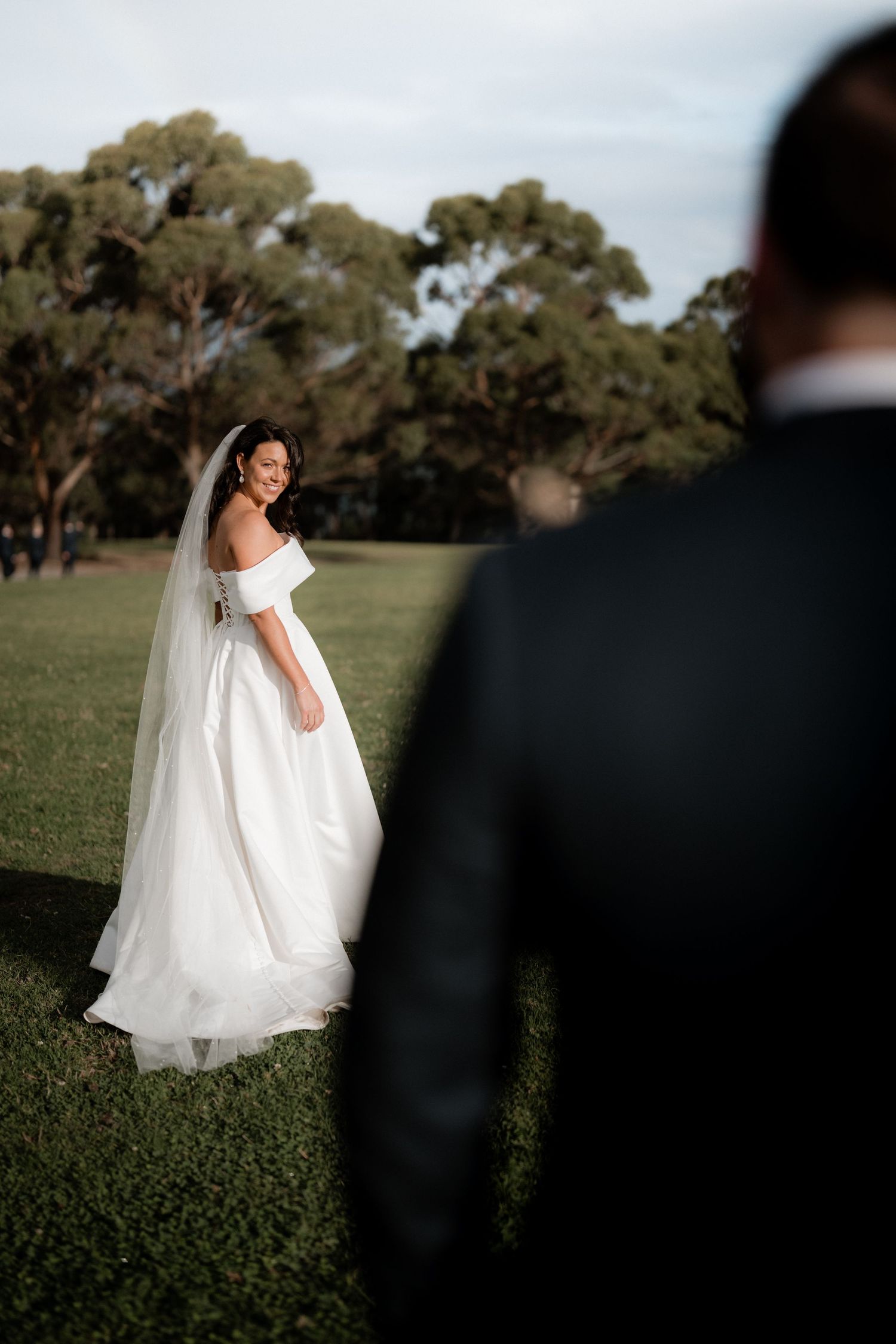 Beautiful wedding couple on grassy field with eucalyptus trees in background during outdoor ceremony.