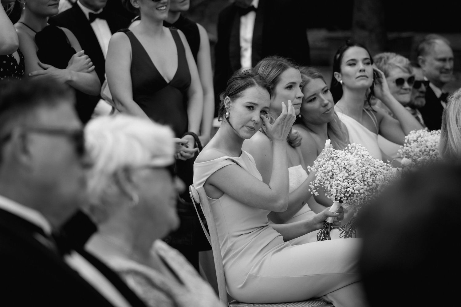 Wedding guests in formal attire seated and enjoying an emotional moment during a black and white ceremony.