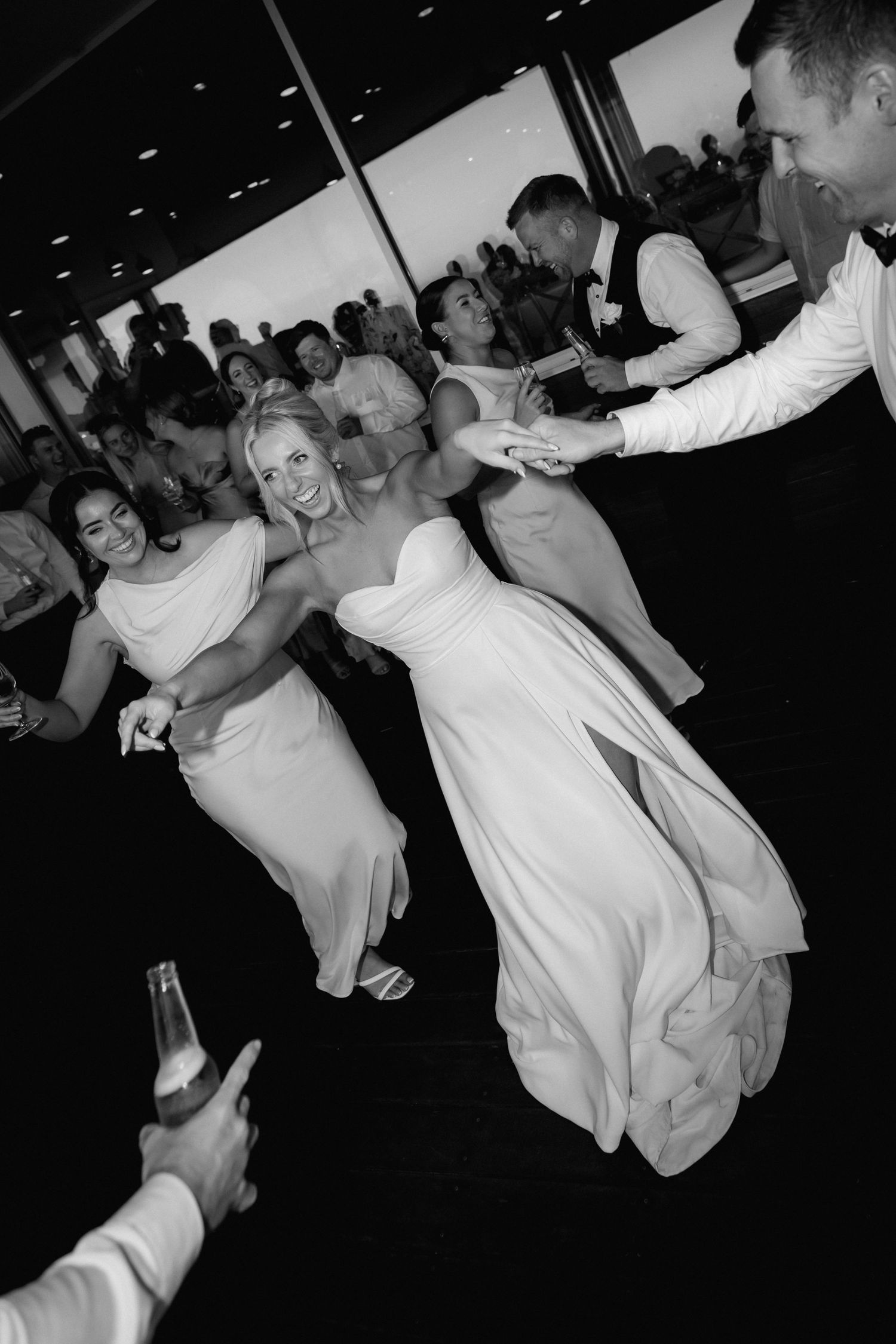 A black and white photo capturing energetic dancing and celebration at a wedding reception.