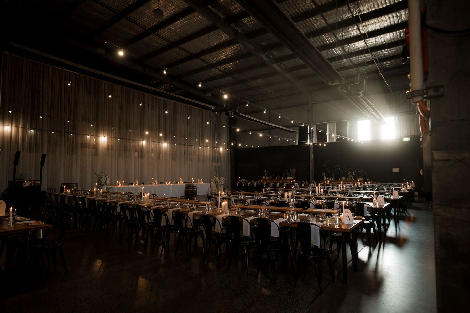 Panoramic view of a dimly lit industrial warehouse venue with exposed beams and hanging lights creating an elegant atmosphere.