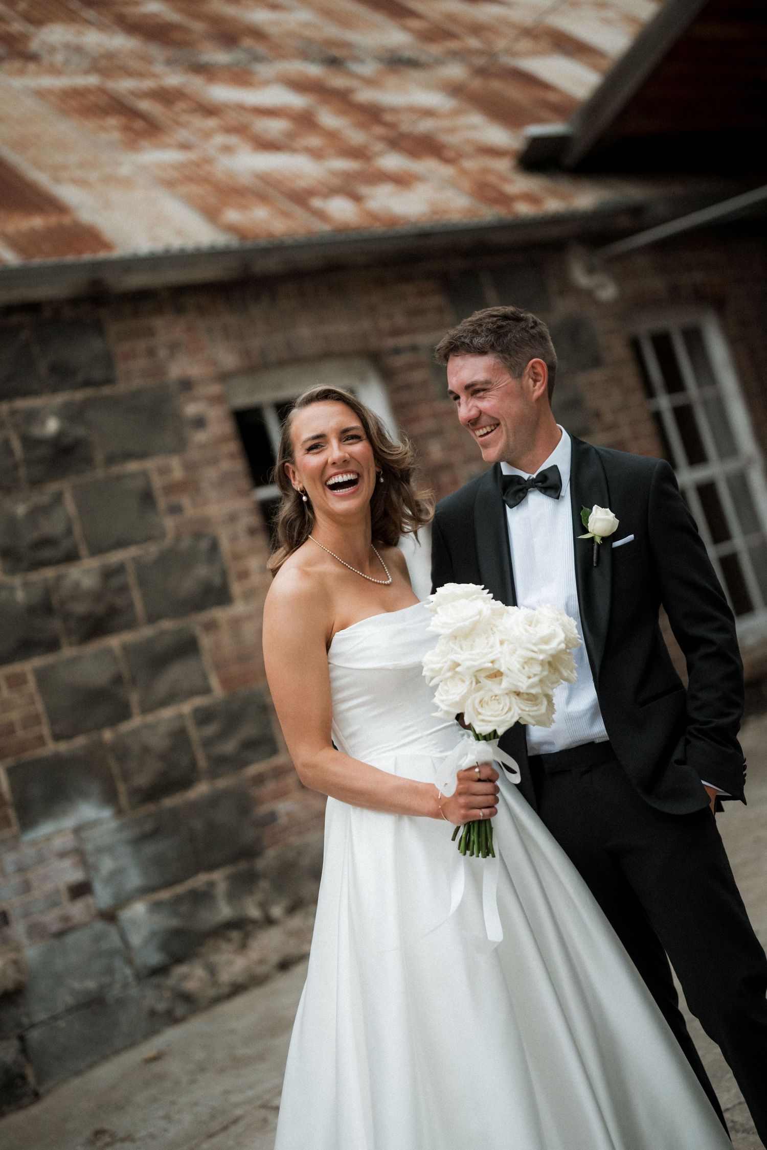 Elegant wedding couple shares joyful moments against rustic brick wall backdrop.
