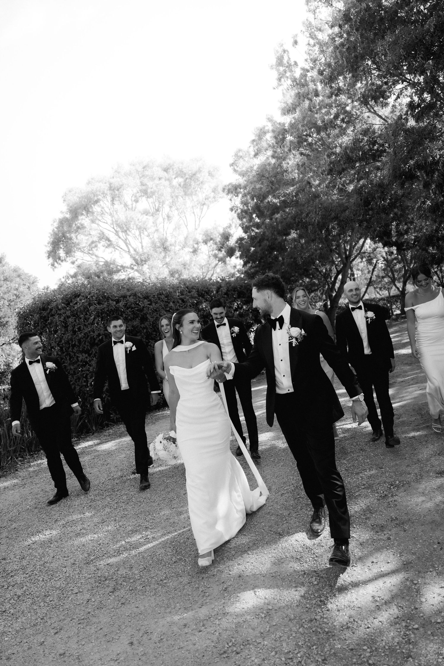 Wedding party in formal attire walks together outdoors in black and white photograph.