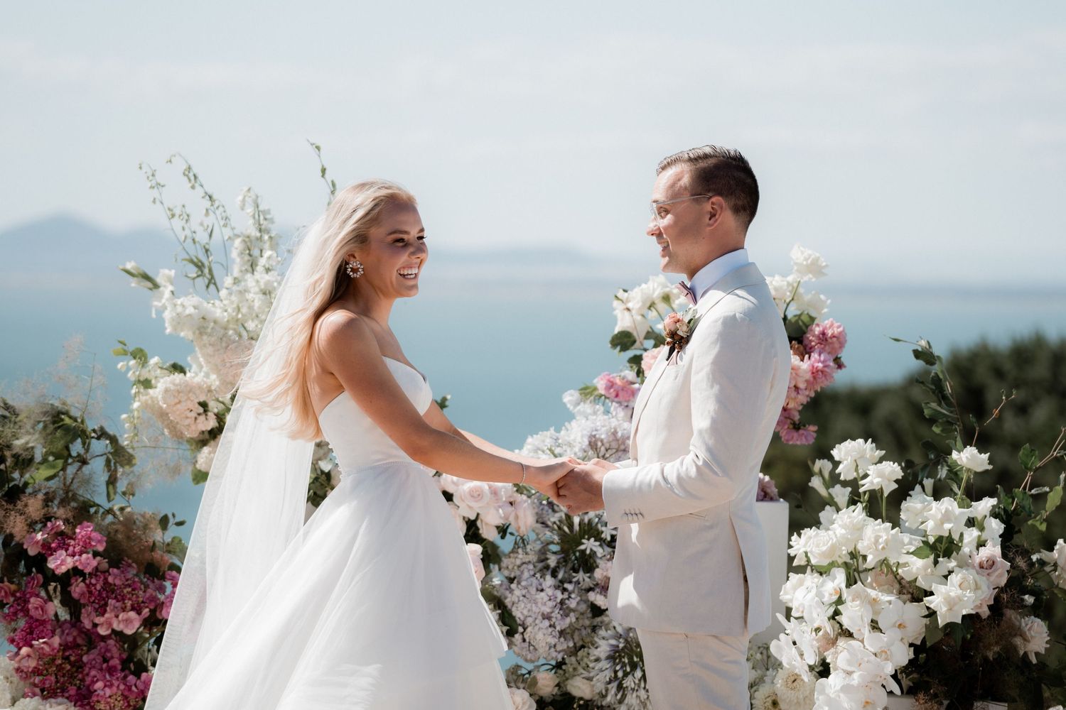 Wedding ceremony setup with white floral arrangements and ocean views in the background.