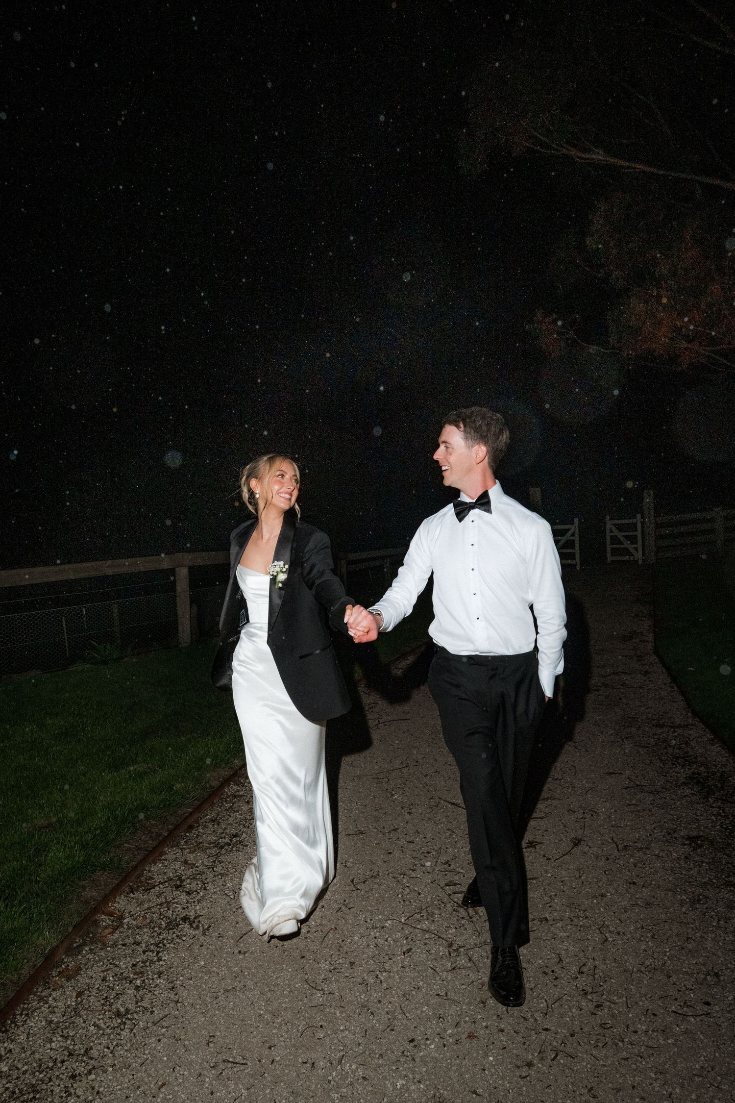 Nighttime wedding photo of couple walking down a gravel path together.