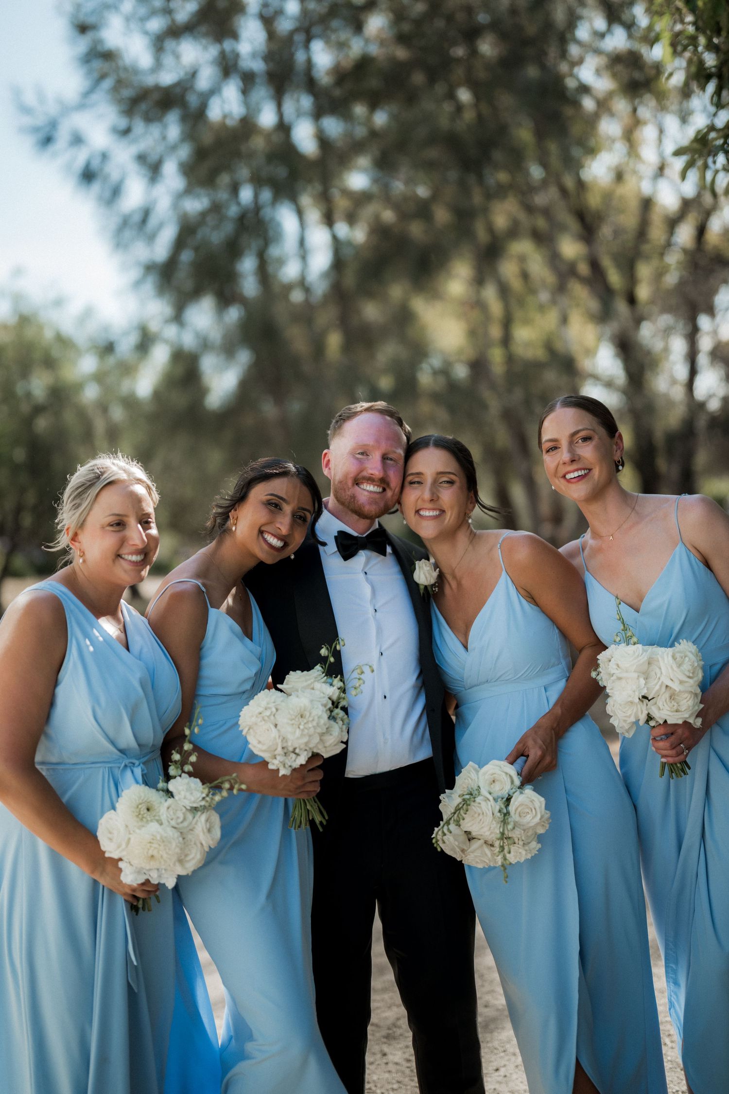 Wedding party in light blue dresses and formal attire posing together outdoors.