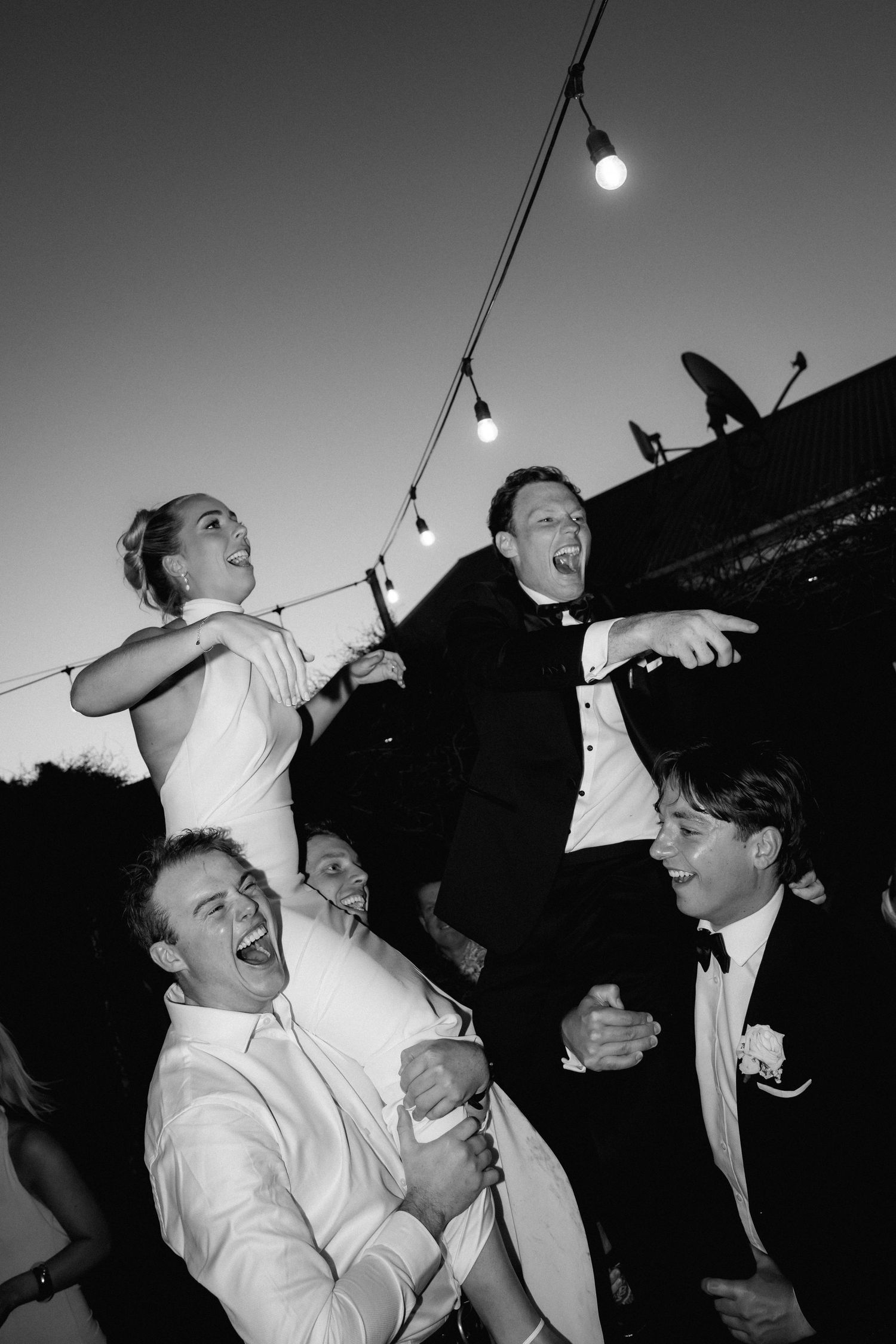 Wedding guests dancing and celebrating at a lively reception party under string lights.
