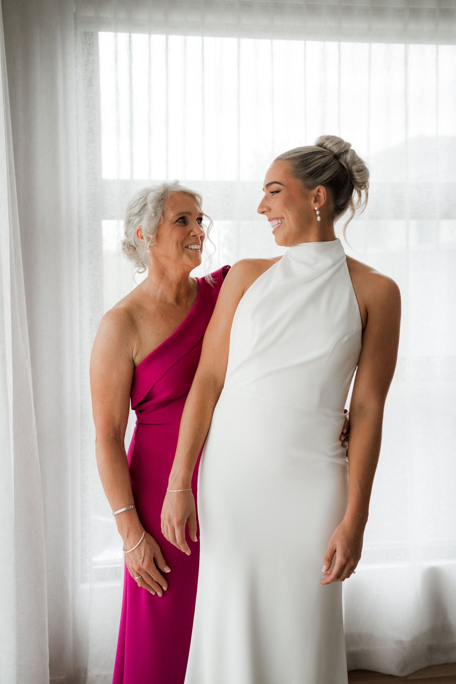 Intimate getting ready moment between wedding party members in a bright room.