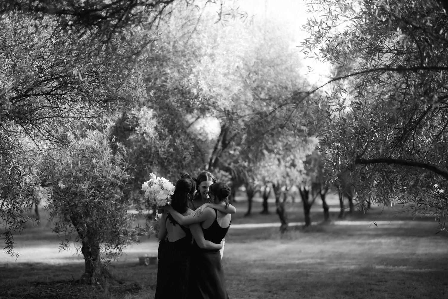 A black and white photograph showing two figures dancing together in a dreamy garden setting with trees.
