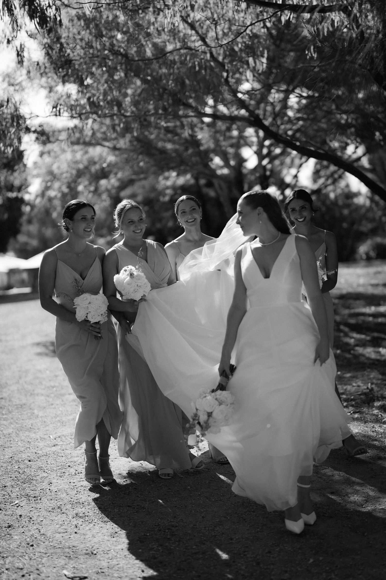 Wedding party members walk together through a shaded outdoor garden path.