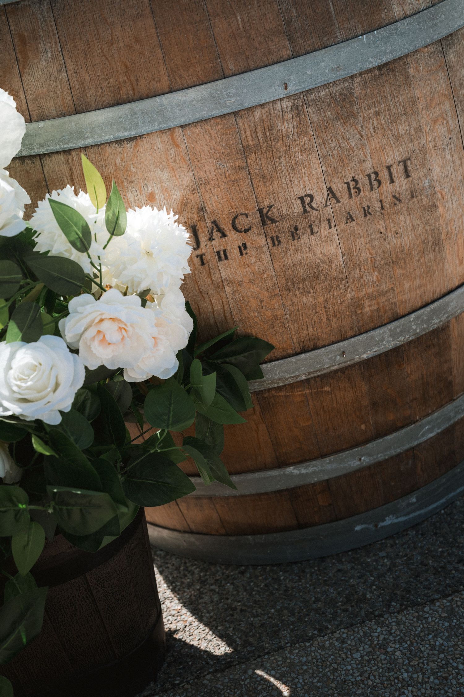 White roses and peonies arranged against a rustic wooden wine barrel.