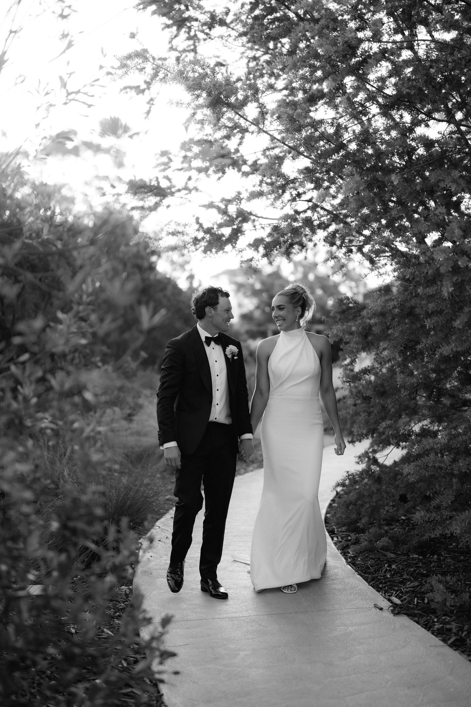 Black and white photo captures wedding party walking along a tree-lined path.