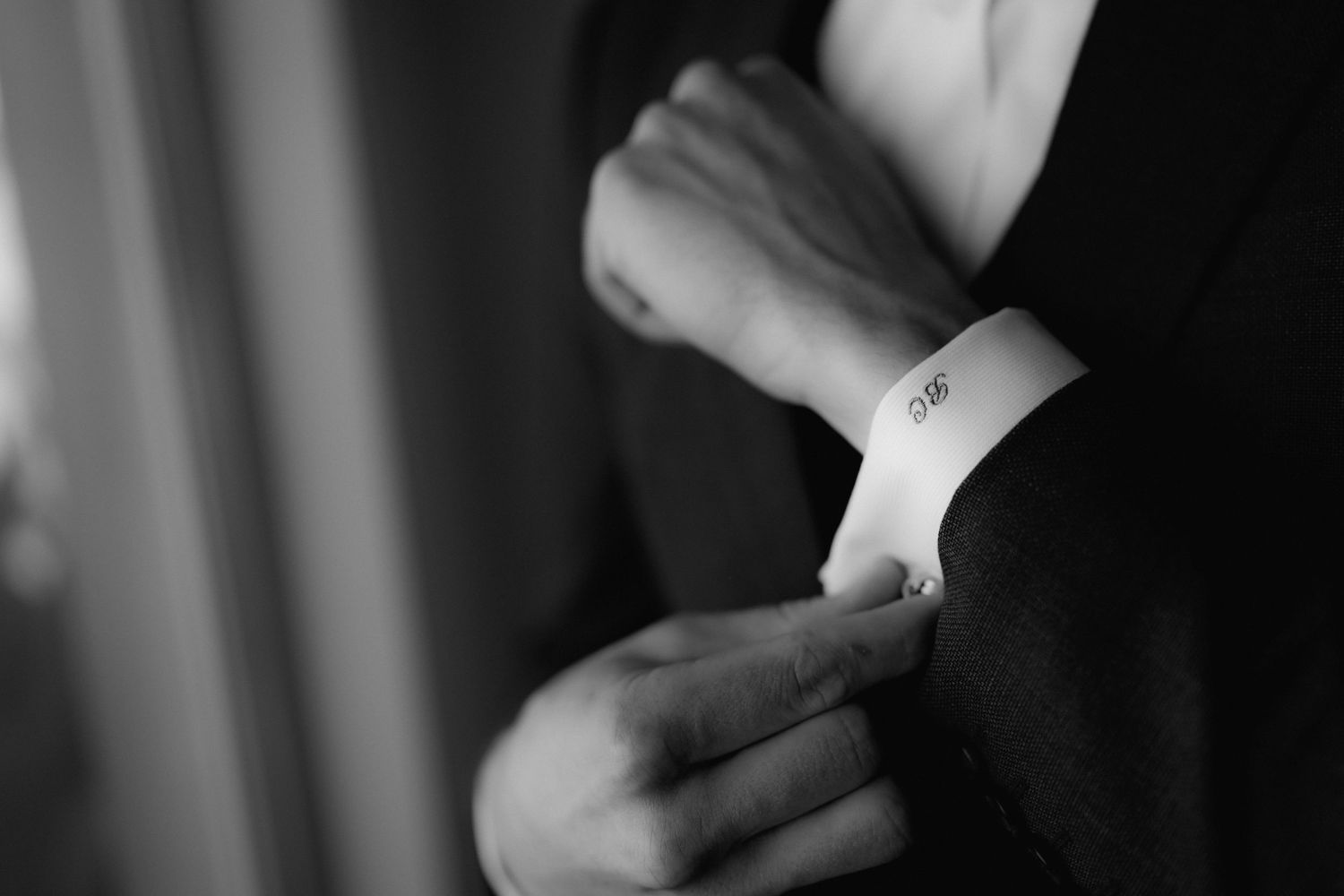Close-up black and white shot of hands adjusting formal shirt cuff and cufflink.