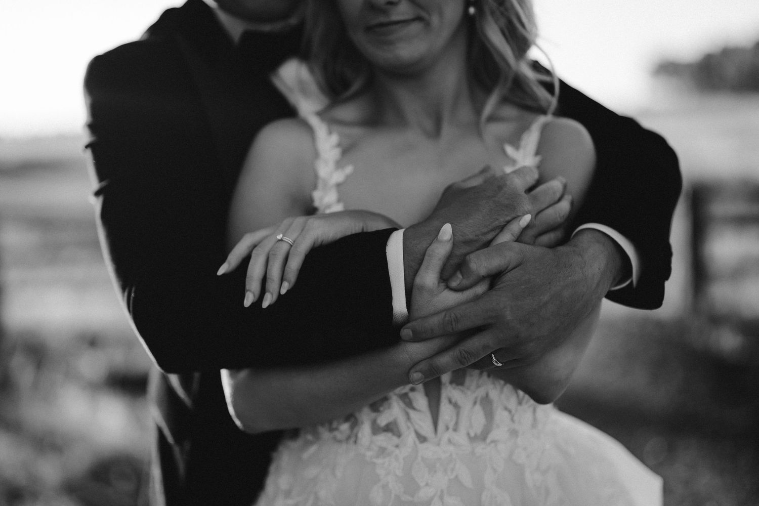 Black and white romantic image of a couple embracing, with the bride wearing a detailed white wedding dress.