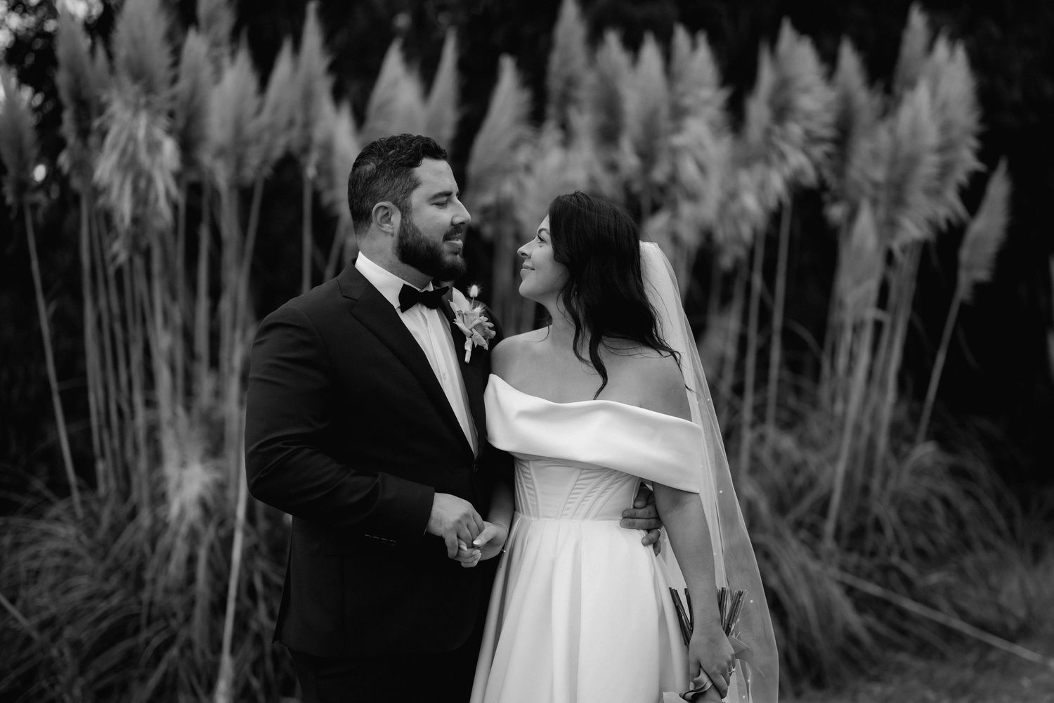 A romantic black and white wedding portrait with pampas grass creating an ethereal backdrop in nature.