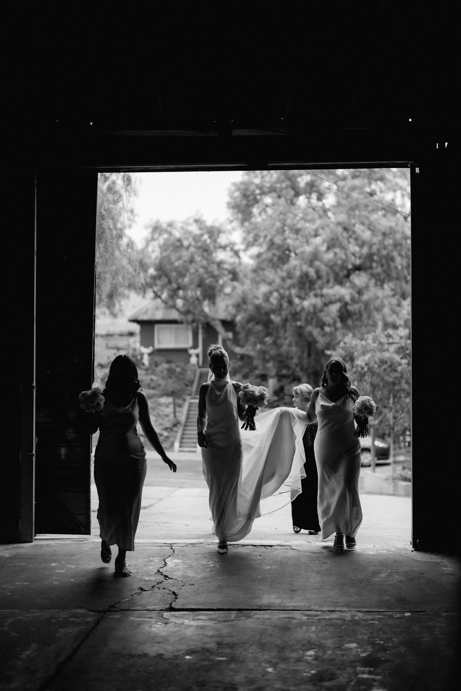 Silhouettes of bridesmaids walking through a doorway holding up a wedding dress train in black and white.