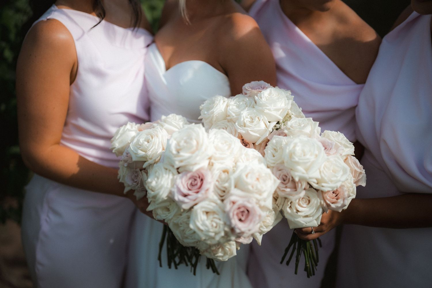 Close-up of elegant white and blush rose wedding bouquets held by bridesmaids in matching dresses.