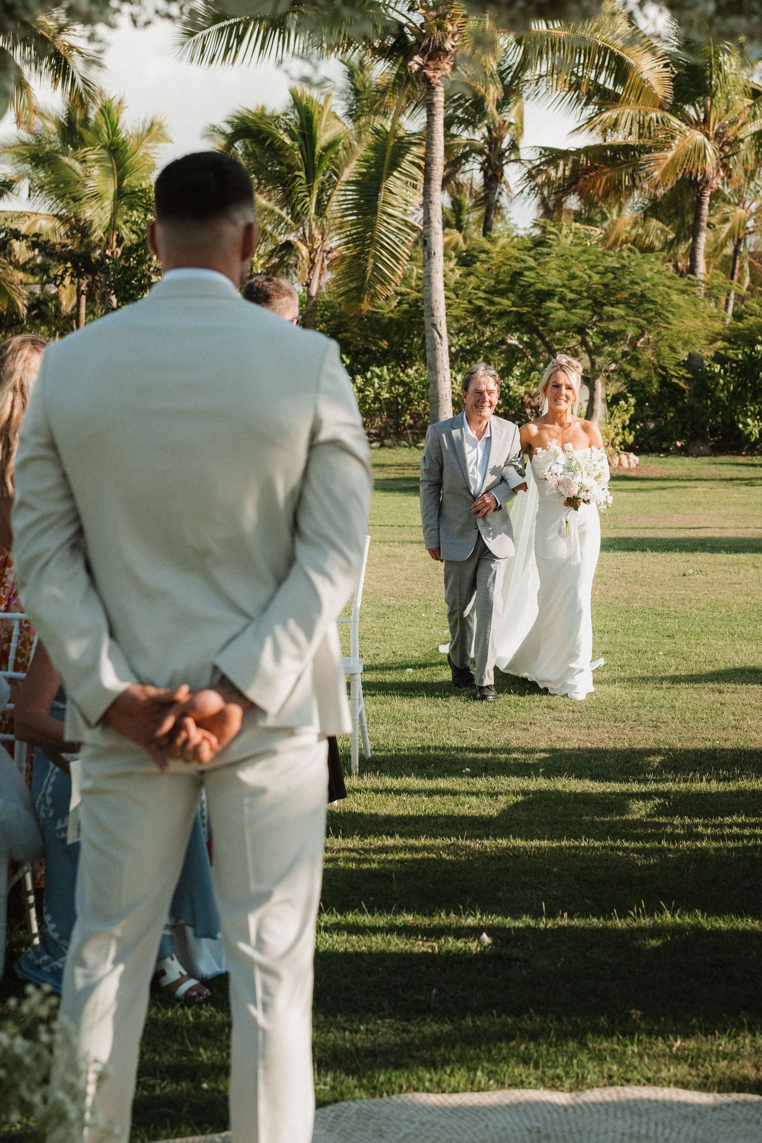 Beachside wedding ceremony with palm trees and guests in tropical setting.