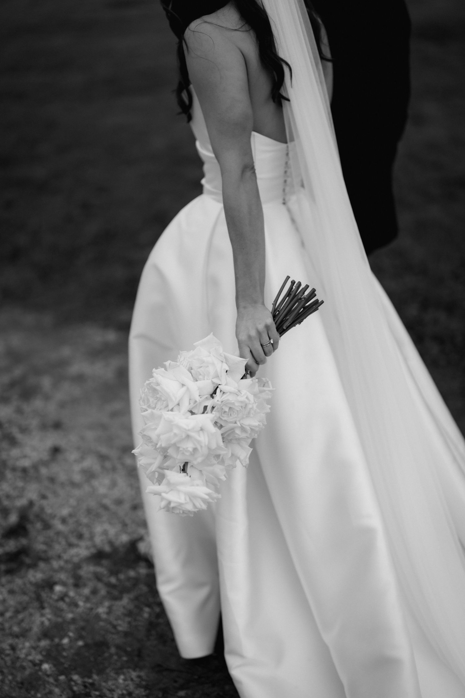 A black and white detail shot of a bride holding her wedding bouquet against her flowing dress.