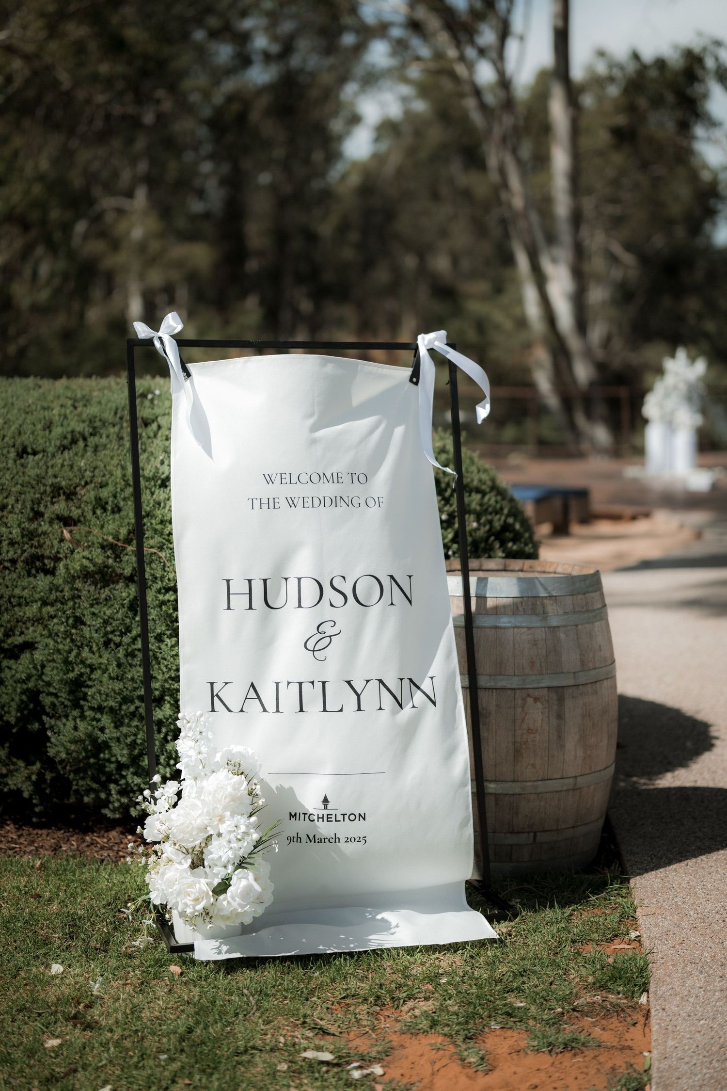 White welcome signs with names displayed outdoors next to rustic wooden barrels.