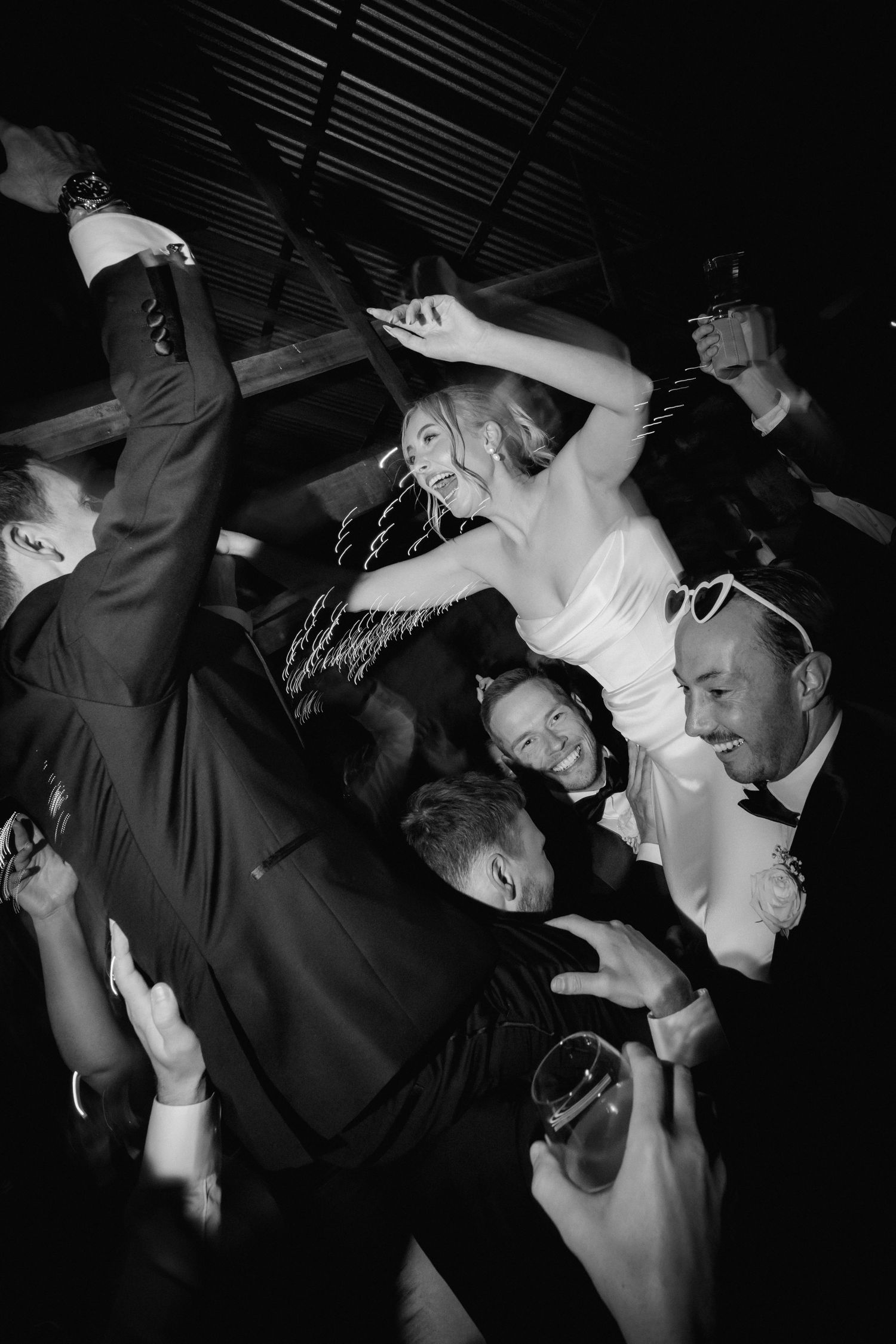 Black and white photo of energetic dancing and celebration at a dark reception venue.