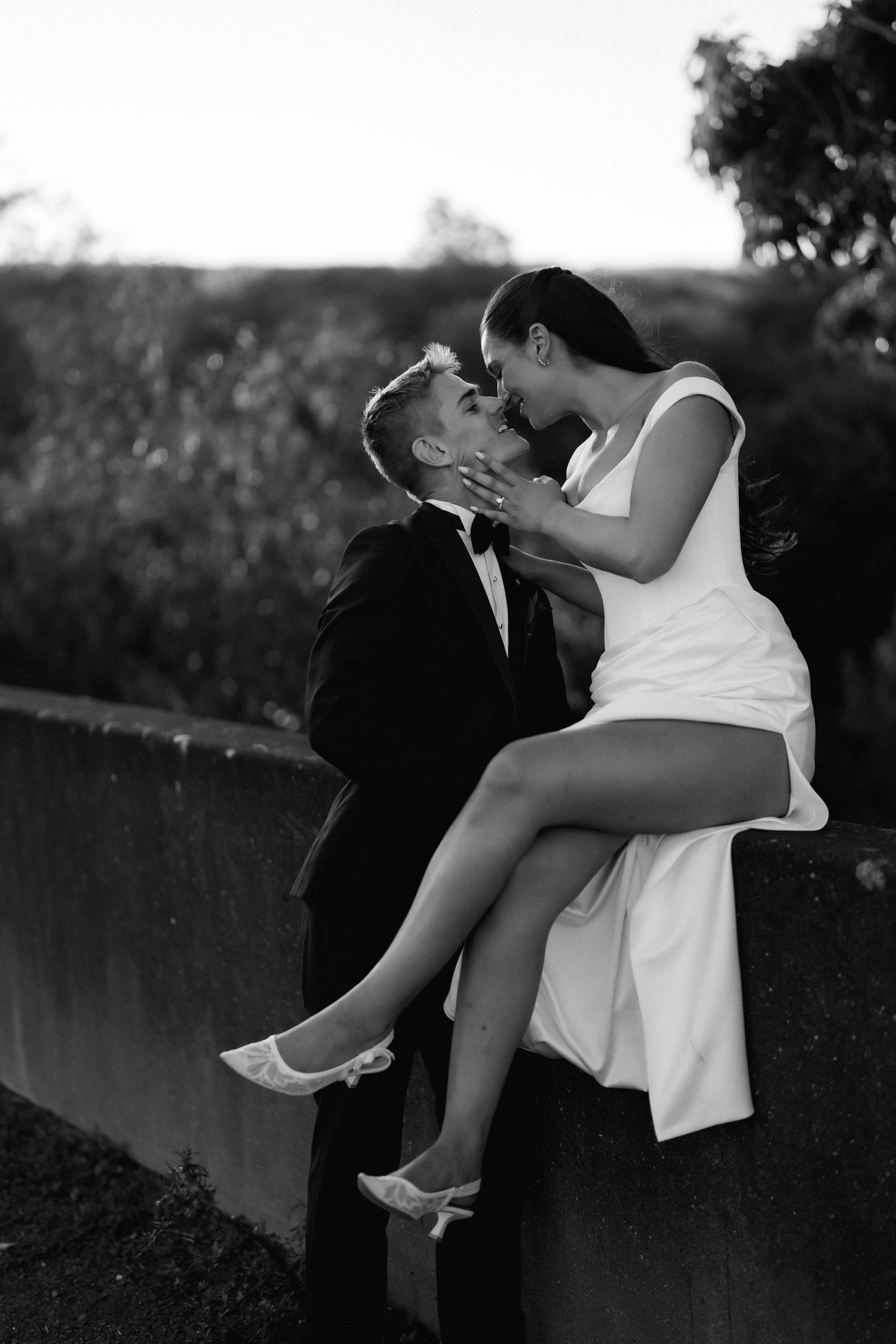 Romantic black and white portrait of couple on stone wall at sunset.