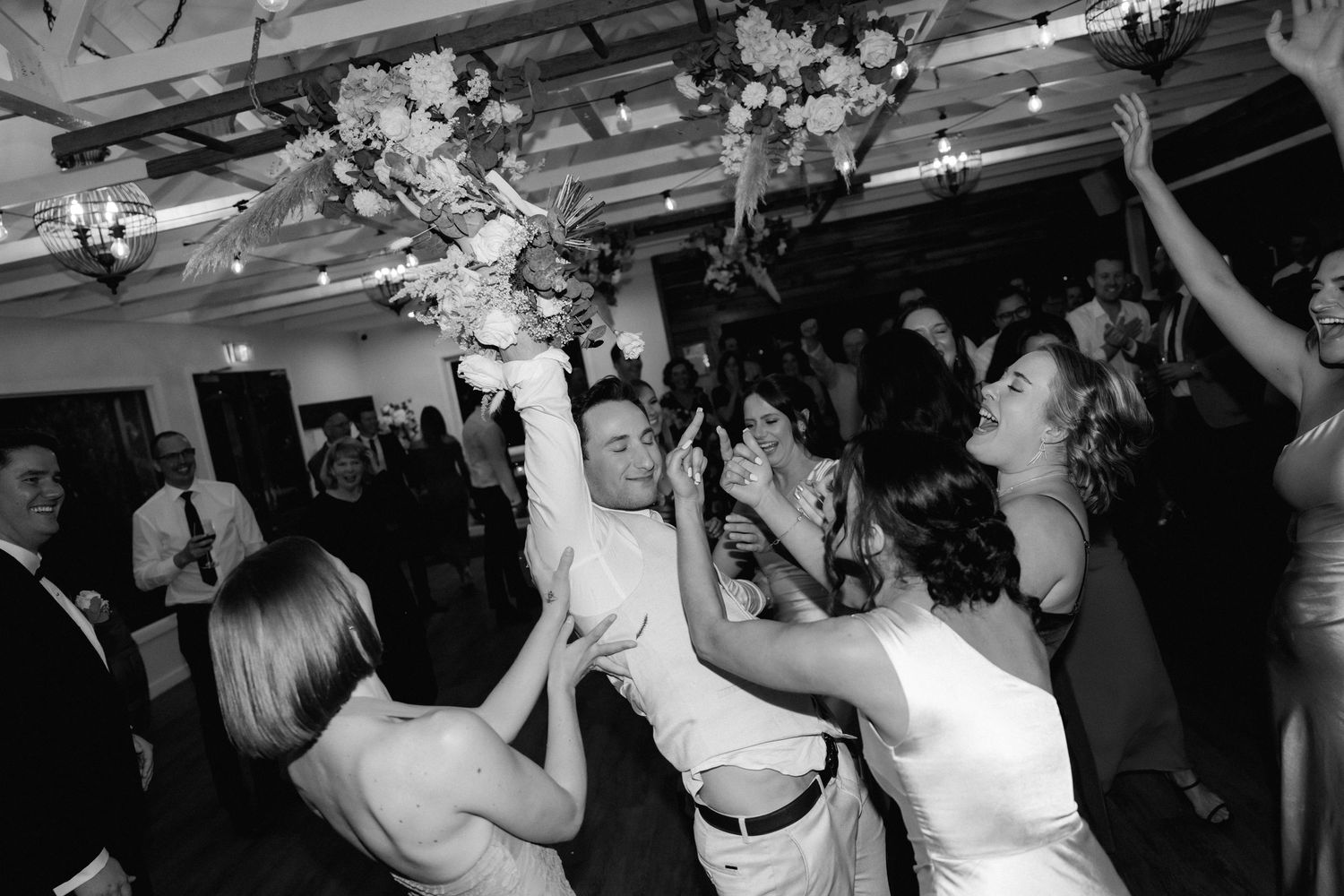 Black and white photography of wedding celebration with people dancing at a lively reception party.