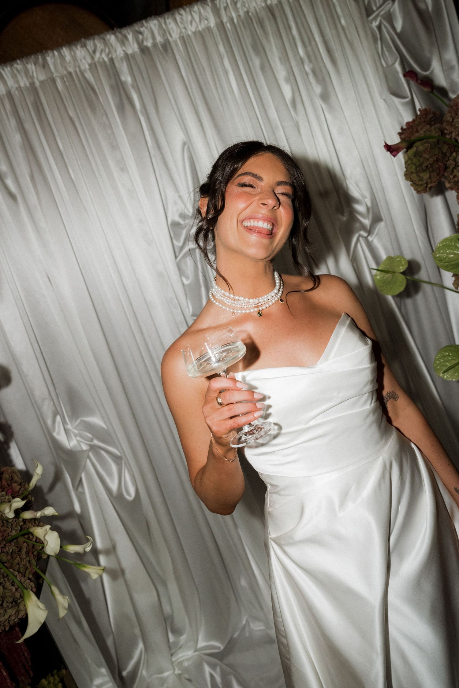 A series of candid shots showing someone in a white dress laughing and holding a champagne glass against a white backdrop.