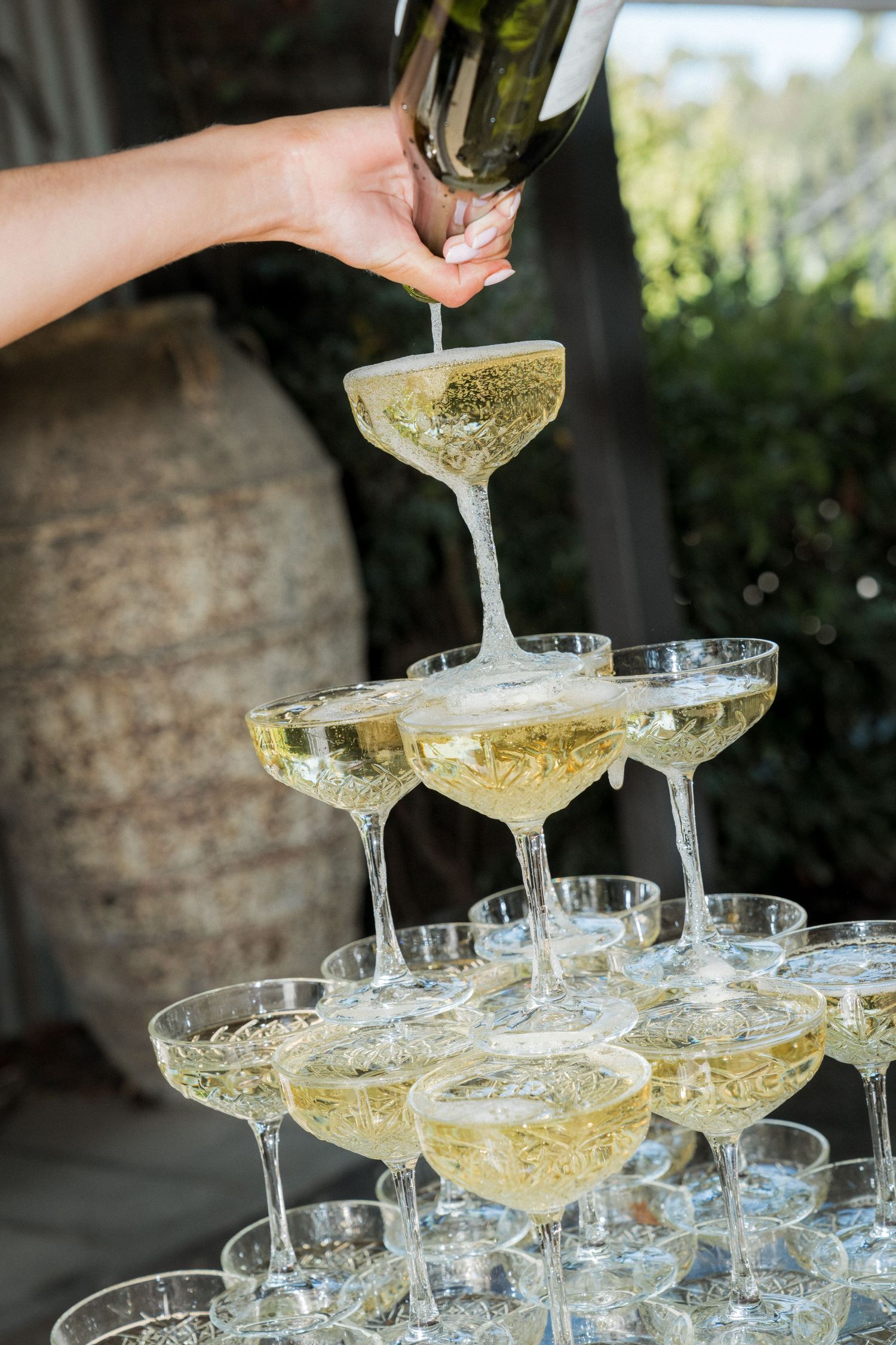 Champagne being poured into a tower of elegant coupe glasses at a wedding reception.