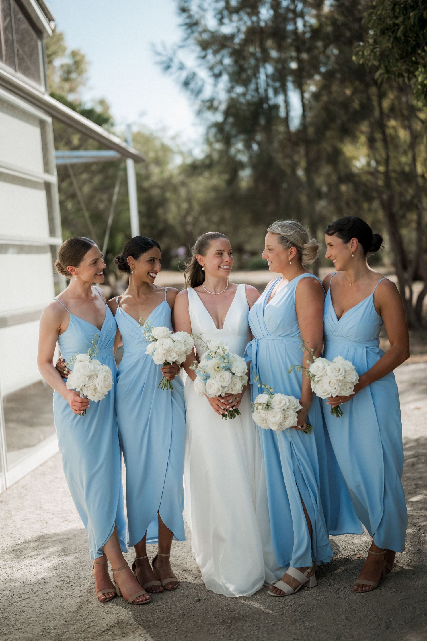 Bridesmaids in light blue dresses pose together holding white bouquets.