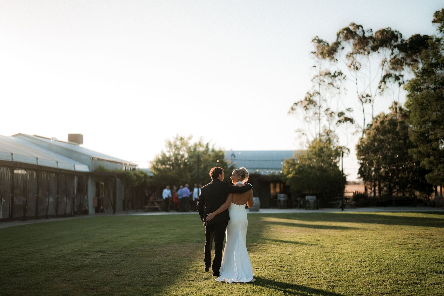 A couple strolls through a sunlit meadow during their wedding photoshoot at sunset.
