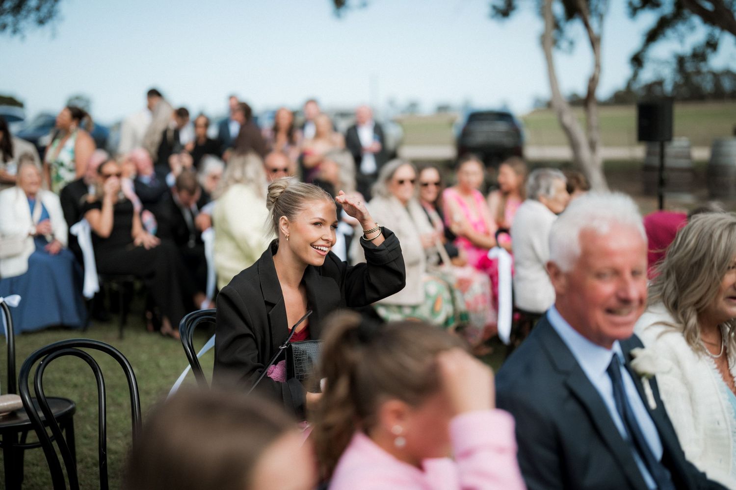 Wedding guests seated outdoors watch a ceremony unfold.