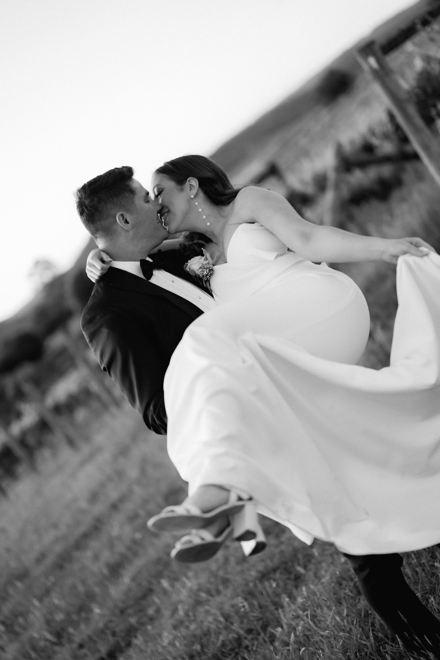 A romantic black and white wedding photo capturing a dramatic dip kiss moment outdoors.
