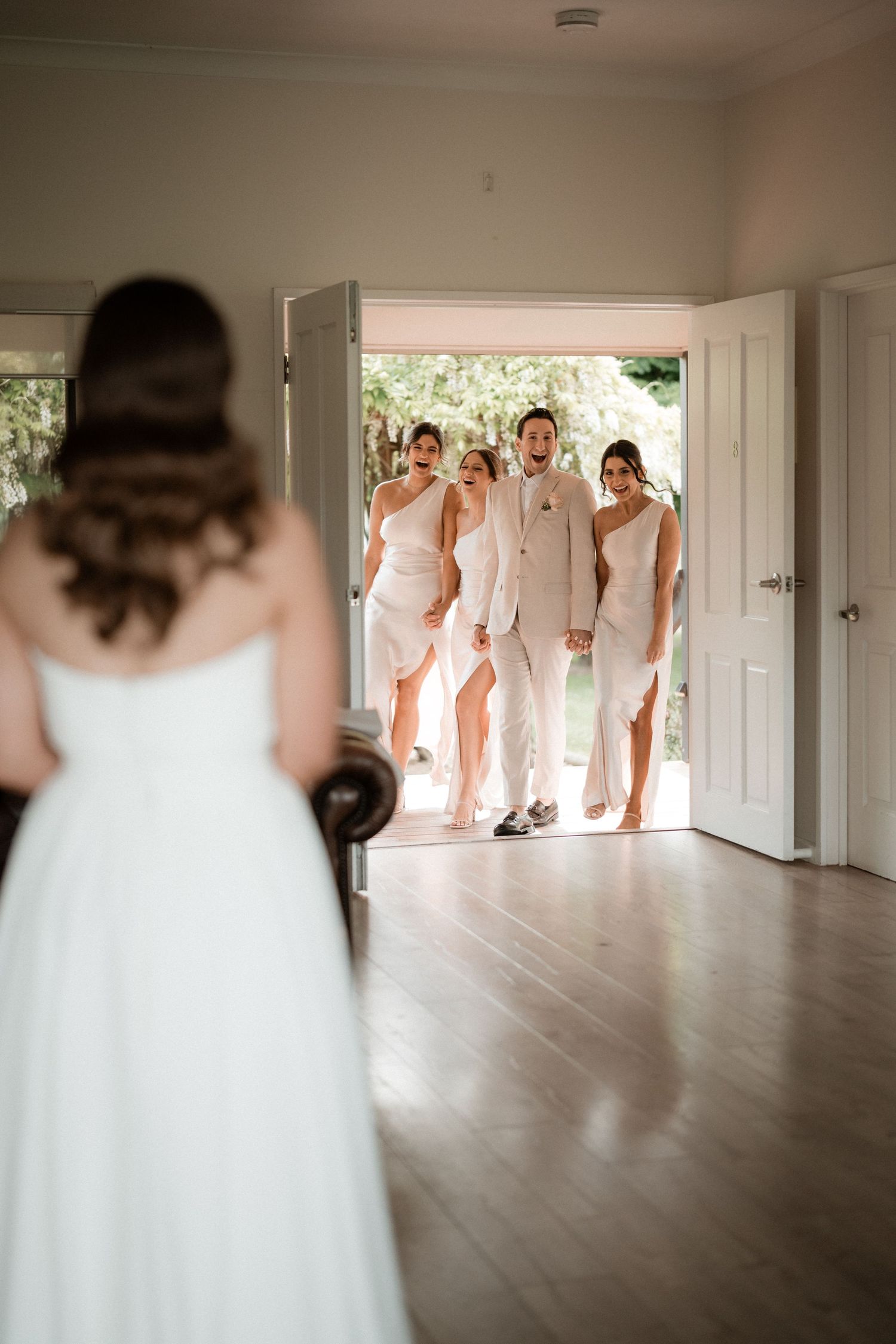 Wedding party first look moment captured in an elegant indoor setting with hardwood floors.