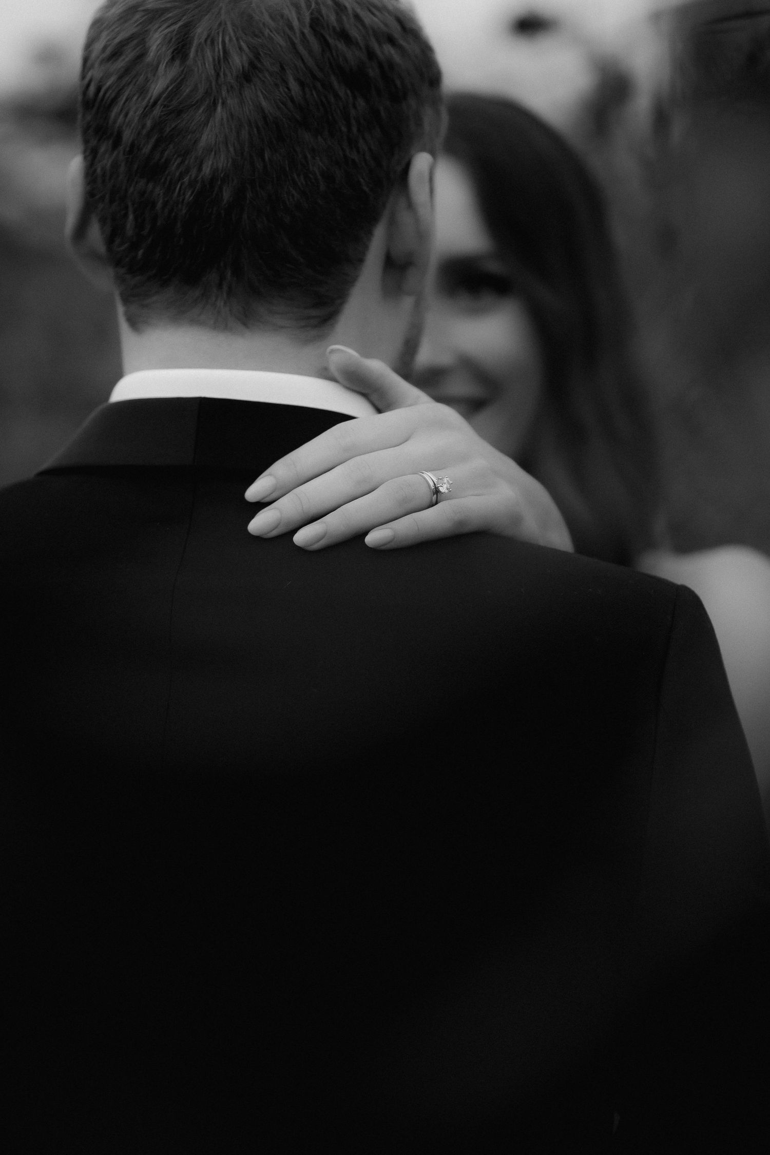 Close-up black and white shot of a diamond ring on hand during an intimate embrace.