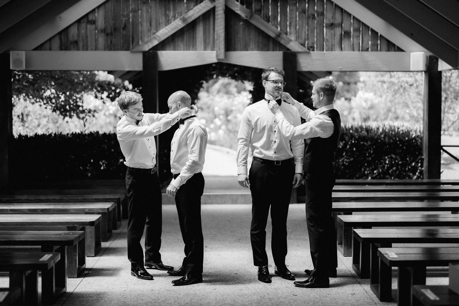 Black and white photo of groomsmen celebrating and jumping in a rustic wooden pavilion during a wedding celebration.